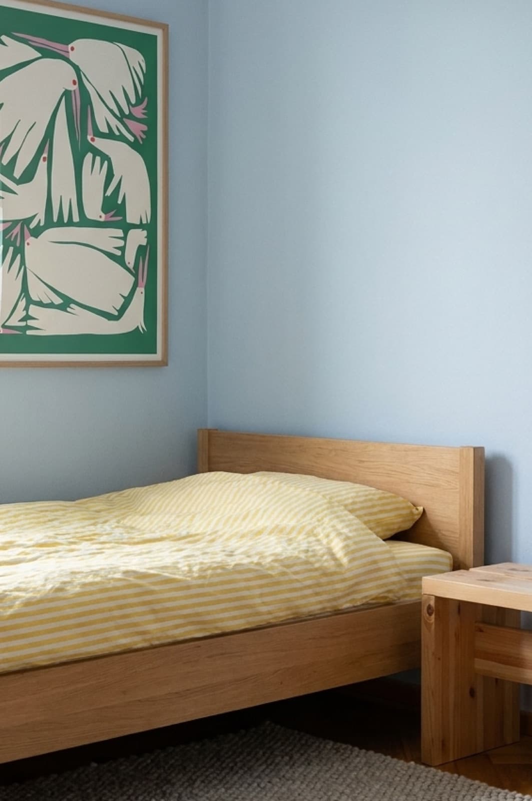 Birdie Green on a pale blue bedroom wall above a light oak bed